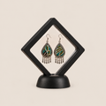 Verdant Reverie earrings displayed inside a transparent, diamond-oriented black frame on a black base.