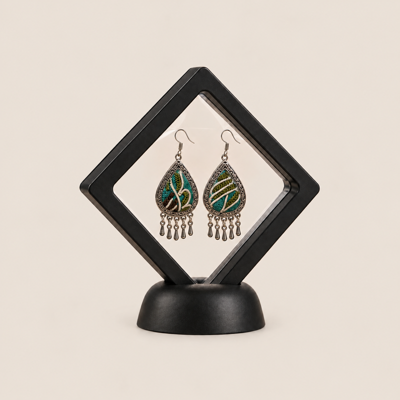 Verdant Reverie earrings displayed inside a transparent, diamond-oriented black frame on a black base.