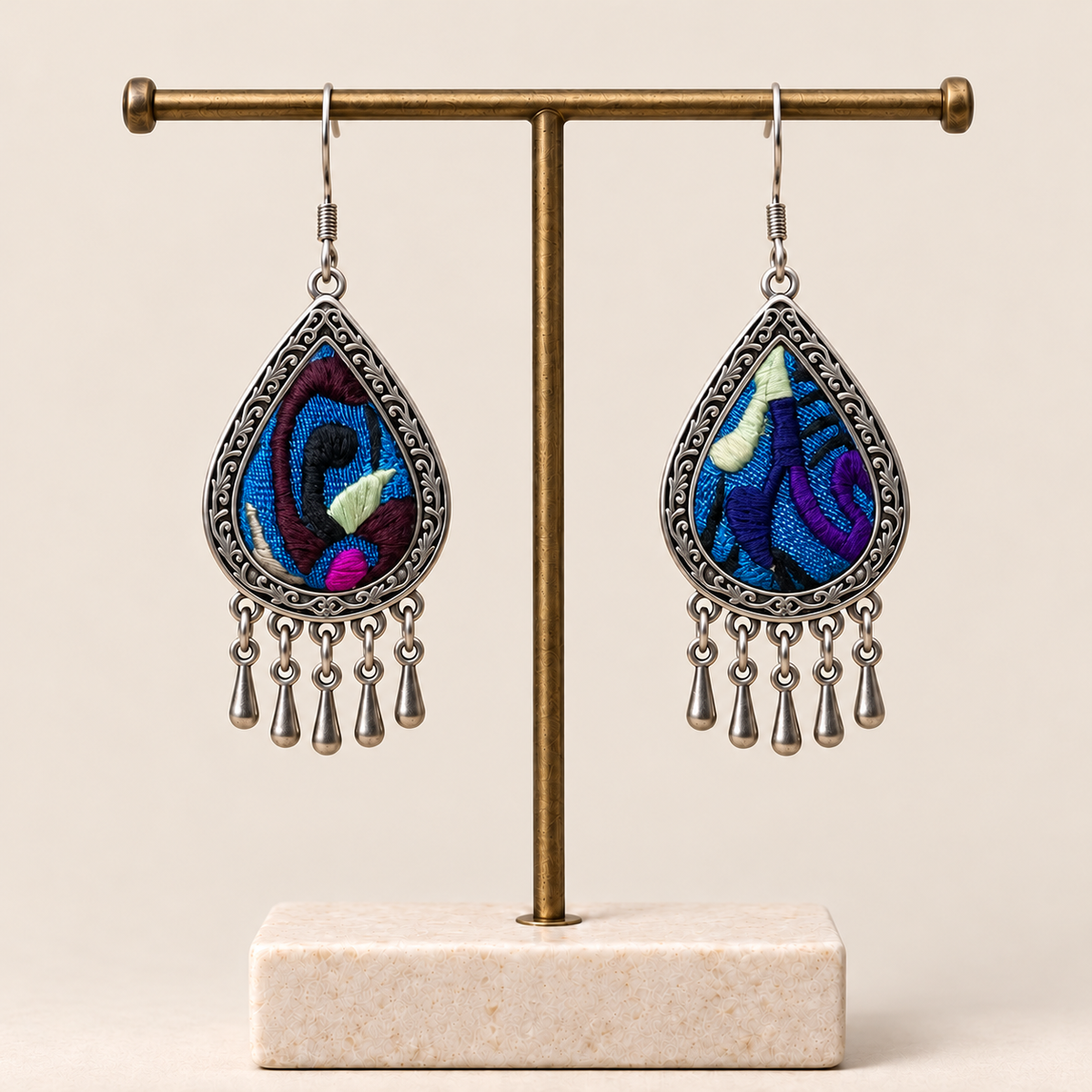 Violet Reverie embroidered teardrop earrings hanging from a T-bar stand, showing differing patterns and five short drops each.