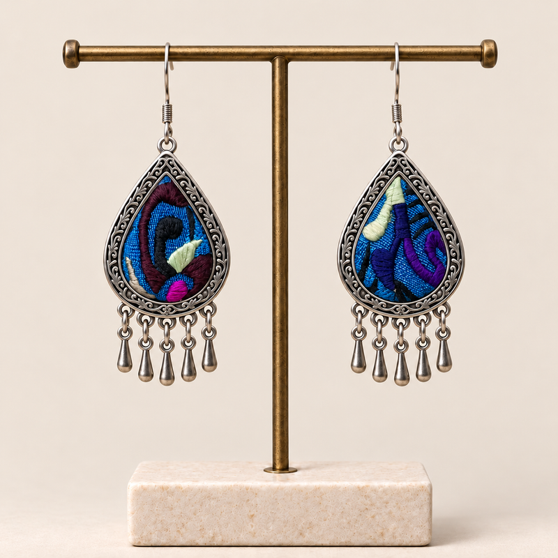 Violet Reverie embroidered teardrop earrings hanging from a T-bar stand, showing differing patterns and five short drops each.