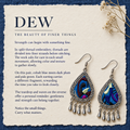 DEW split-thread embroidery story panel titled The beauty of finer things, with Violet Reverie earrings on cream paper over blue cloth beside dried flowers.