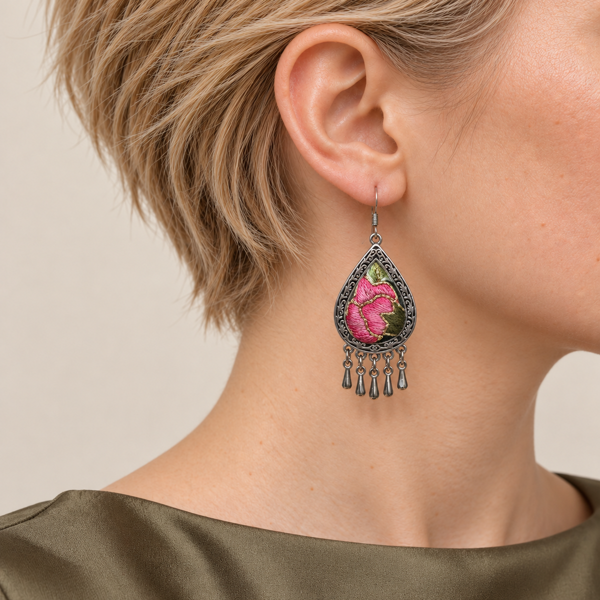 Close-up of a Petal Serenade earring worn with pink petals, green leaves and fine gold-colored outlines facing outward.