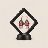 Petal Serenade earrings displayed inside a transparent, diamond-oriented black frame on a black base.