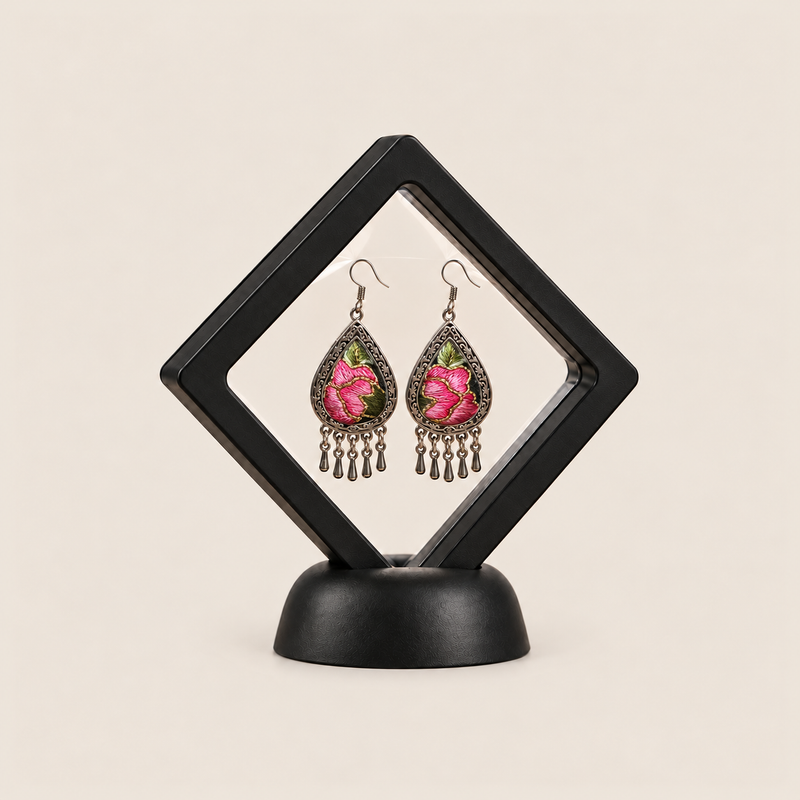 Petal Serenade earrings displayed inside a transparent, diamond-oriented black frame on a black base.