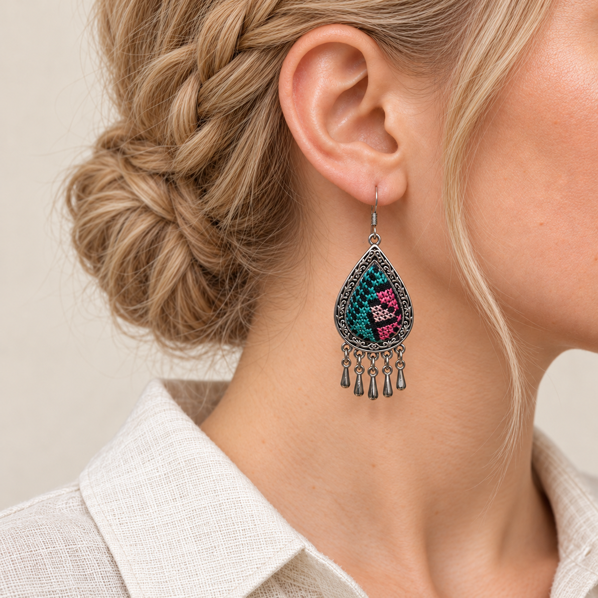 Close-up of a Twilight Mosaic earring worn with teal, pink and pale geometric stitches on black textile facing outward.