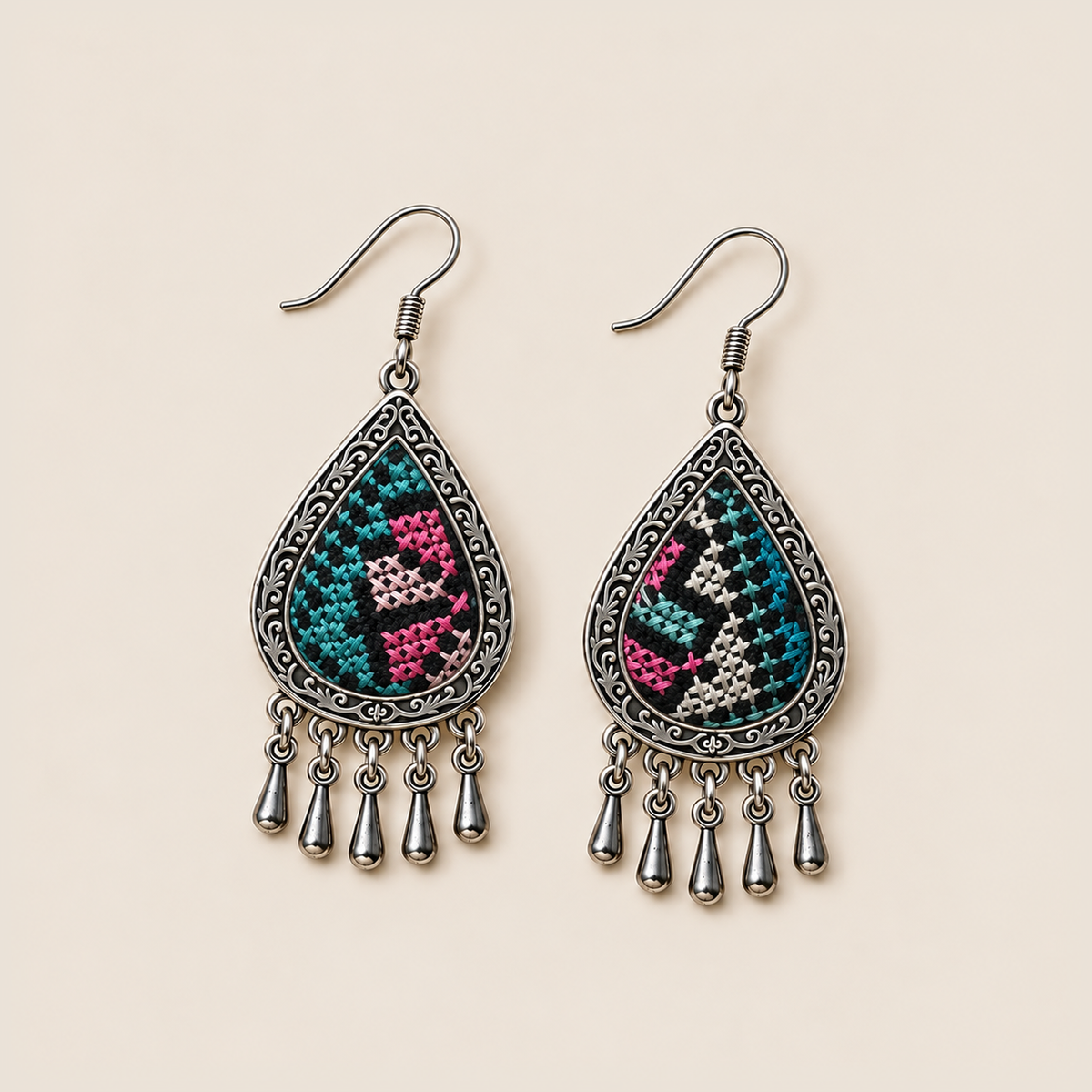 Twilight Mosaic earrings laid flat, showing different teal, pink and pale geometric embroidery patterns on black textile.
