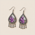 Lavender Sonata earrings laid flat, showing purple petals with dark purple outlines and small green and brown accents on pale textile.