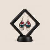 Prismatic Reverie earrings displayed inside a clear diamond-shaped frame with a black border and base.