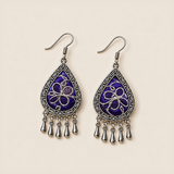 Violet Arabesque earrings lying face up, showing differing silver-white stitched curves across the purple pair.