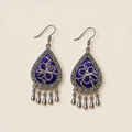 Violet Arabesque earrings lying face up, showing differing silver-white stitched curves across the purple pair.