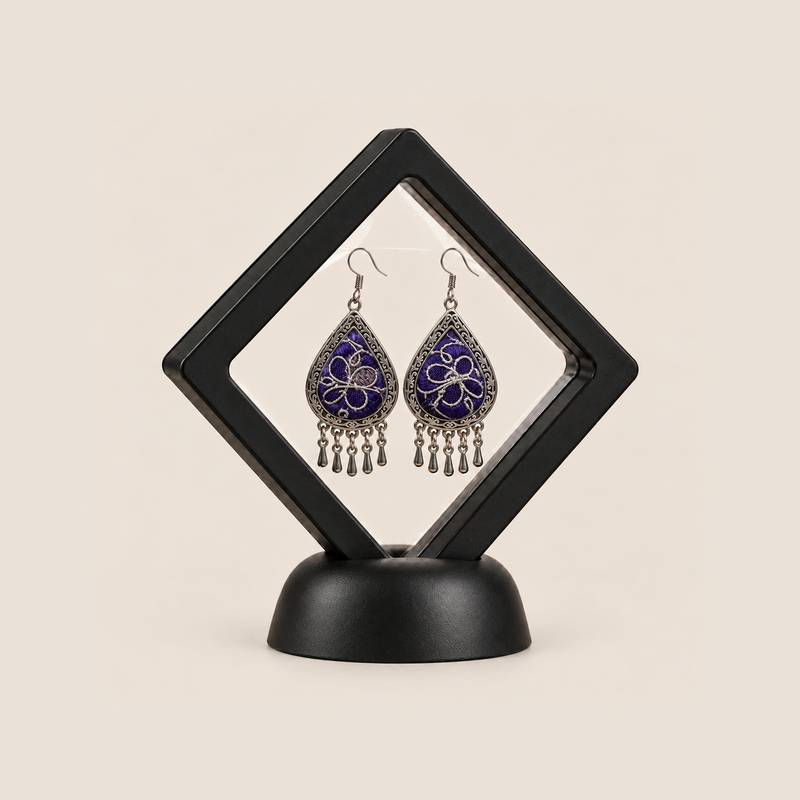 Violet Arabesque earrings displayed inside a clear diamond-shaped frame with a black border and base.