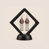 Burgundy Nocturne long tassel earrings displayed inside a clear diamond-shaped frame with a black border and base.