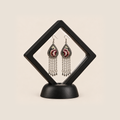 Burgundy Nocturne long tassel earrings displayed inside a clear diamond-shaped frame with a black border and base.
