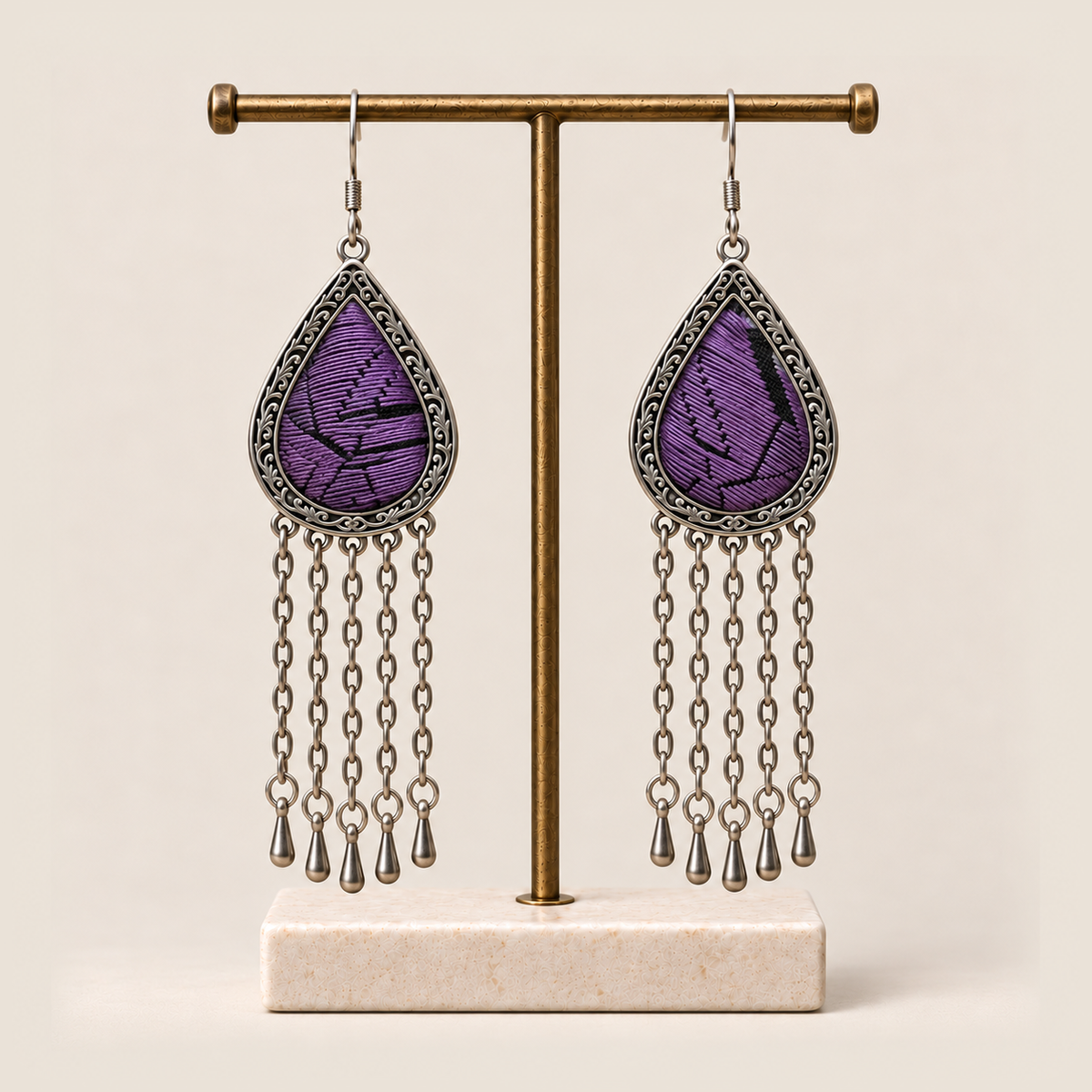 Amethyst Cadence earrings hanging from a T-bar stand with five long chains and teardrop ends beneath each embroidered frame.