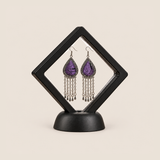 Amethyst Cadence long tassel earrings displayed inside a clear diamond-shaped frame with a black border and base.