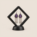 Amethyst Cadence long tassel earrings displayed inside a clear diamond-shaped frame with a black border and base.