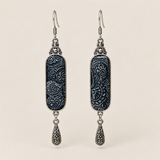 Indigo Stillness batik long drop earrings with pale spirals on dark textile and one engraved teardrop beneath each panel.