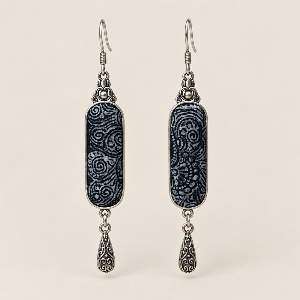Indigo Stillness batik long drop earrings with pale spirals on dark textile and one engraved teardrop beneath each panel.