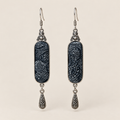 Indigo Stillness batik long drop earrings with pale spirals on dark textile and one engraved teardrop beneath each panel.
