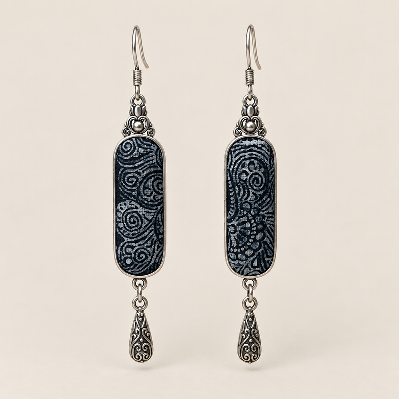 Indigo Stillness batik long drop earrings with pale spirals on dark textile and one engraved teardrop beneath each panel.