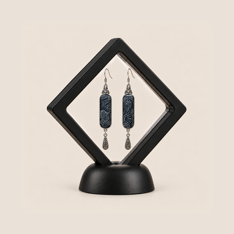 Indigo Stillness batik earrings presented inside a black diamond-shaped display frame.