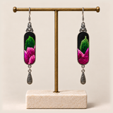 Verdant Blush green and pink embroidered earrings hanging from a gold-tone stand with a pale rectangular base.