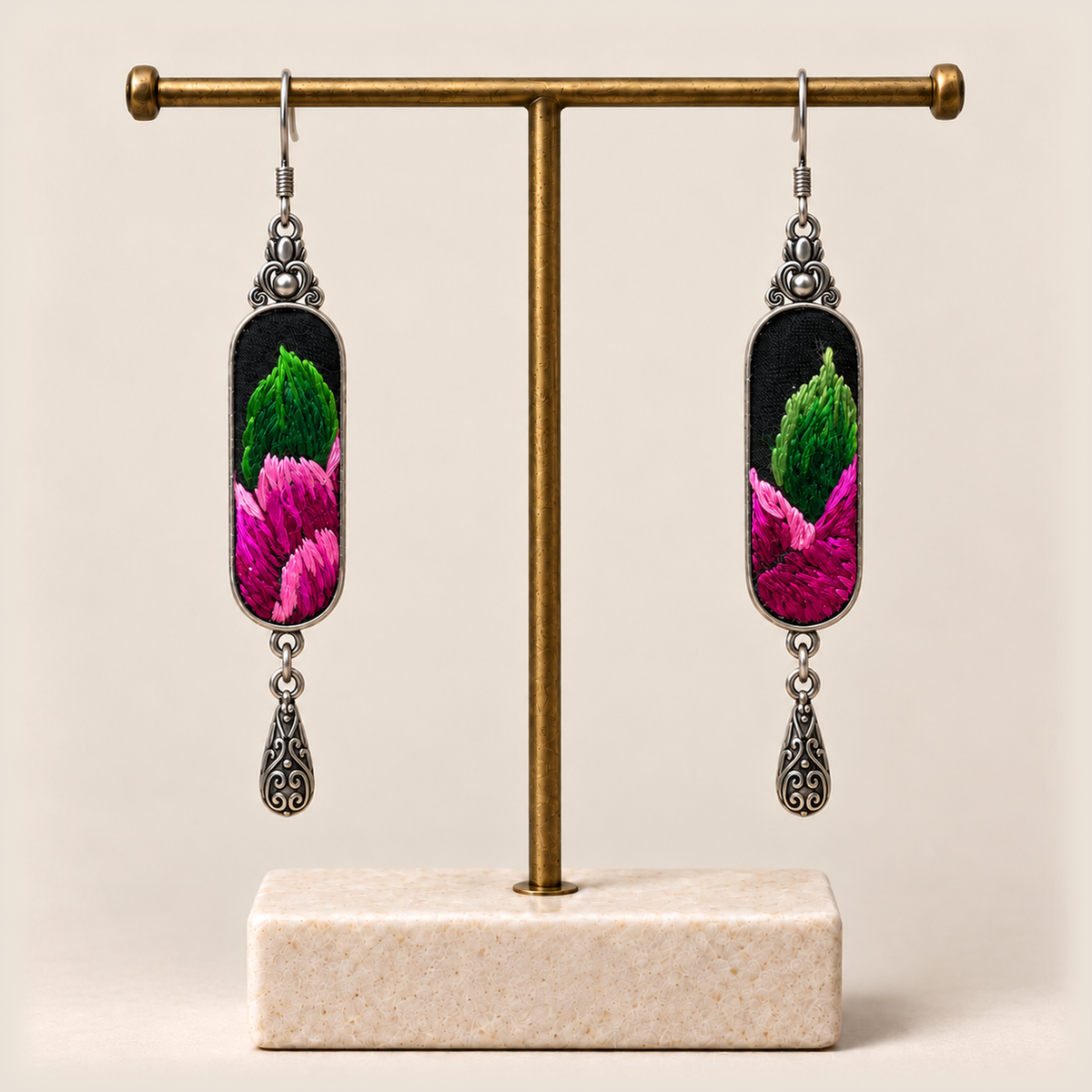 Verdant Blush green and pink embroidered earrings hanging from a gold-tone stand with a pale rectangular base.