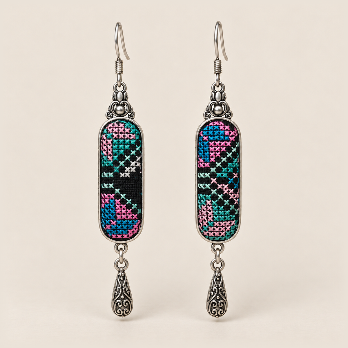Pastel Cadence counted-thread embroidery earrings with pink, teal and blue geometric stitches on black and one teardrop each.