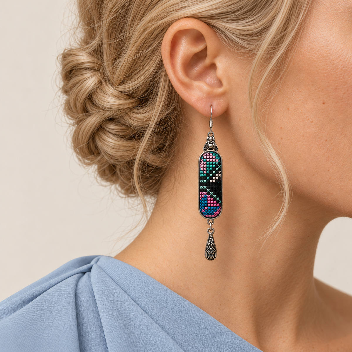 Pastel Cadence earring worn with pink, teal and pale geometric stitching facing forward above a single engraved teardrop.