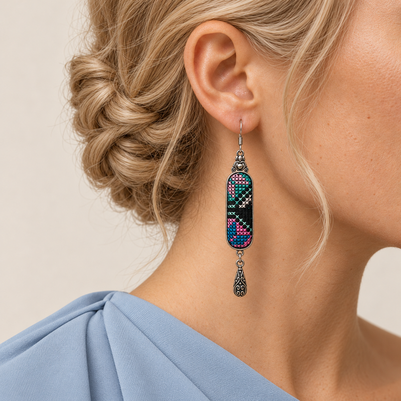 Pastel Cadence earring worn with pink, teal and pale geometric stitching facing forward above a single engraved teardrop.