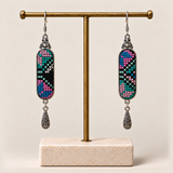 Pastel Cadence embroidered earrings hanging from a gold-tone display stand with a pale rectangular base.