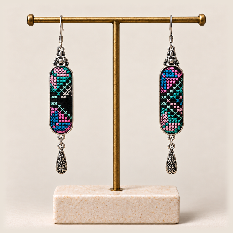 Pastel Cadence embroidered earrings hanging from a gold-tone display stand with a pale rectangular base.