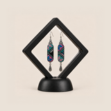Pastel Cadence embroidered earrings inside a black diamond-shaped display frame on a matching base.