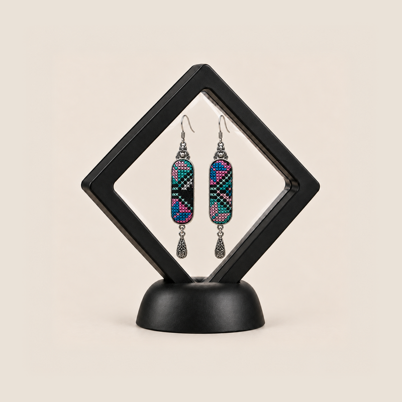 Pastel Cadence embroidered earrings inside a black diamond-shaped display frame on a matching base.