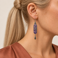 Violet Luminance earring worn with purple stitching with pale looping outlines facing forward above a single teardrop.