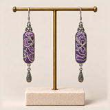 Violet Luminance embroidered earrings hanging from a gold-tone display stand with a pale rectangular base.