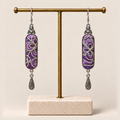 Violet Luminance embroidered earrings hanging from a gold-tone display stand with a pale rectangular base.