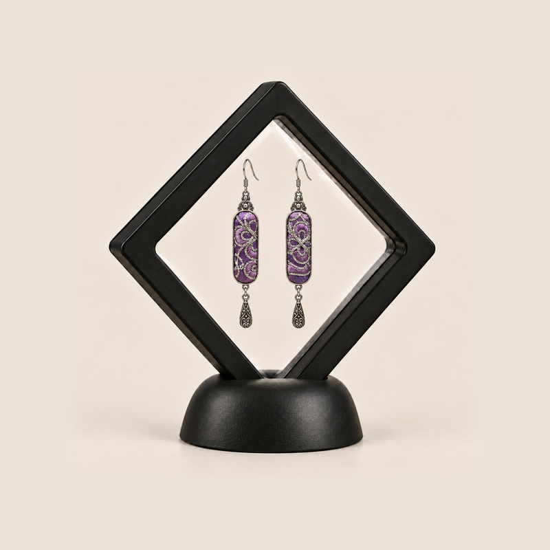 Violet Luminance earrings inside a black diamond-shaped display frame on a matching base.