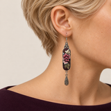 Petal Nocturne earring worn with rose-pink petals and pale, olive-toned foliage on dark textile facing forward above a single teardrop.