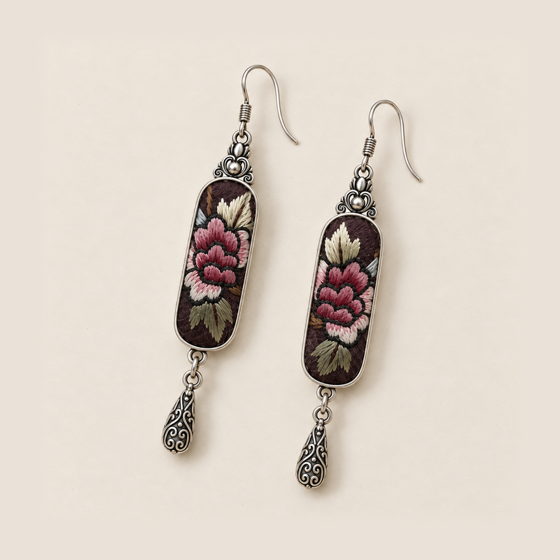Front detail of Petal Nocturne earrings showing layered rose-pink petals and pale, olive-toned leaves on dark panels.