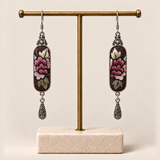 Petal Nocturne embroidered earrings hanging from a gold-tone display stand with a pale rectangular base.