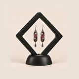 Petal Nocturne earrings inside a black diamond-shaped display frame on a matching base.