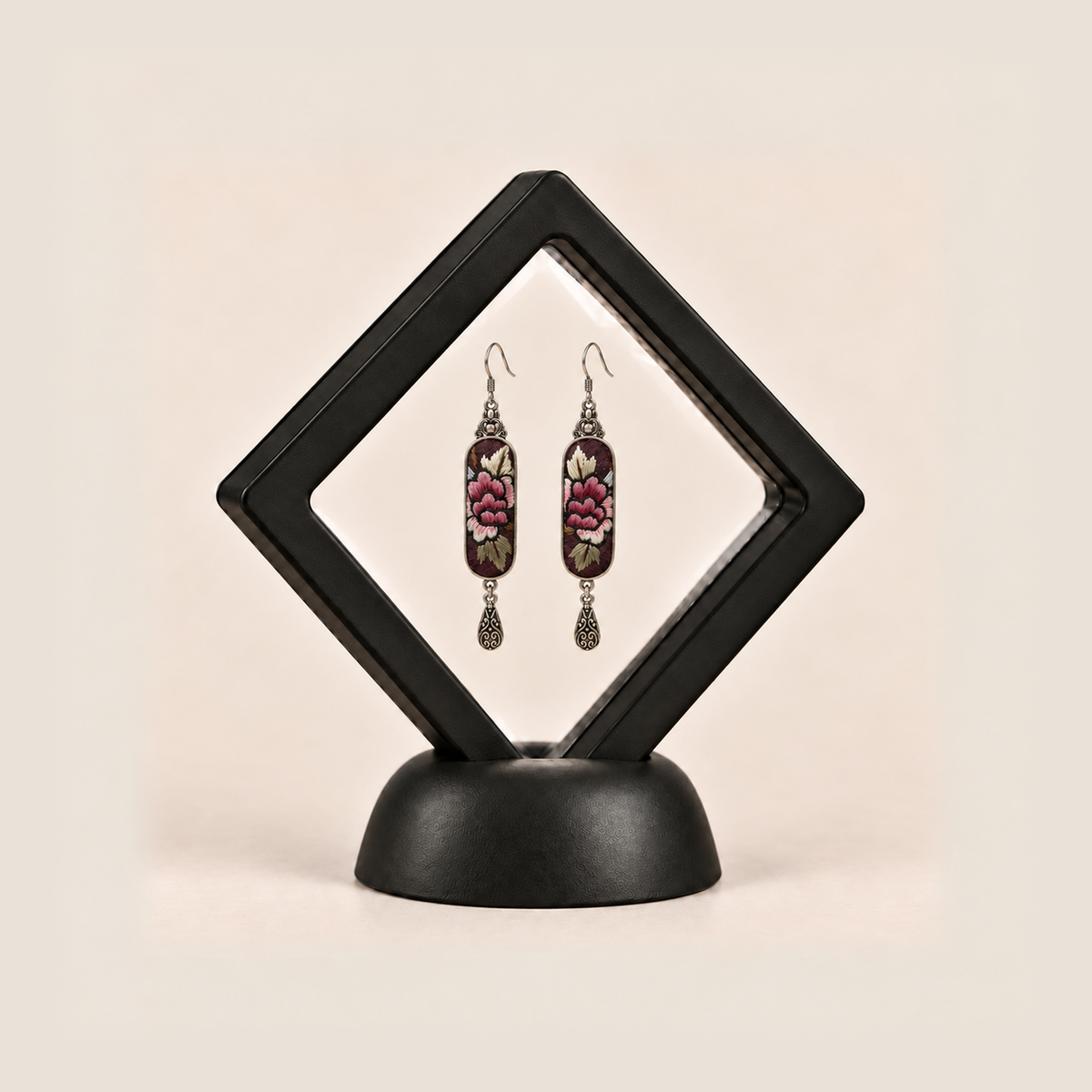 Petal Nocturne earrings inside a black diamond-shaped display frame on a matching base.