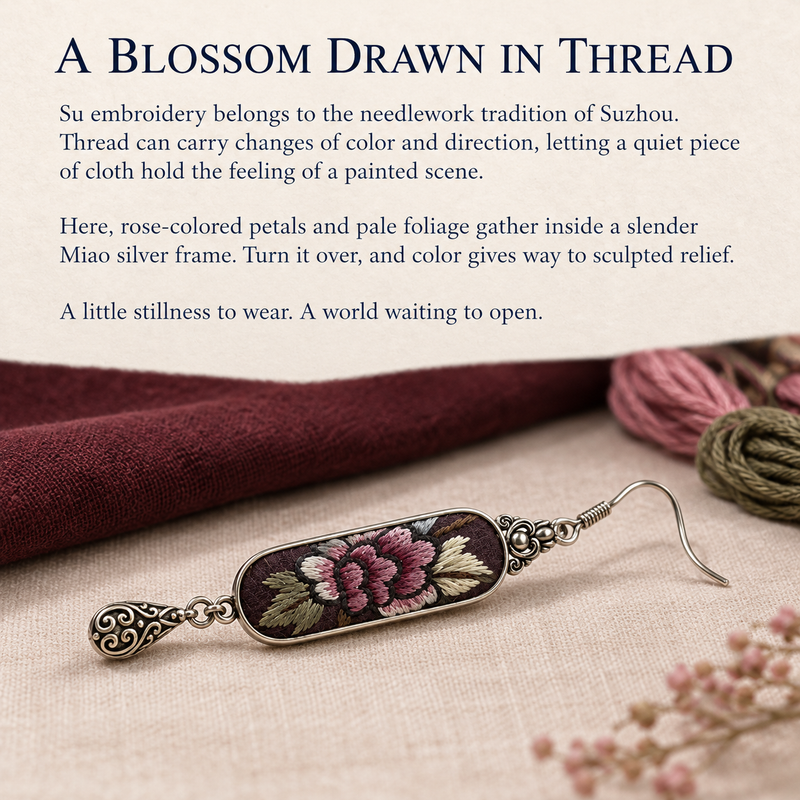 Suzhou Embroidery story card with a Petal Nocturne earring beside burgundy cloth, pink and olive thread and dried flowers.