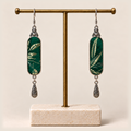 Emerald Reverie Song Brocade earrings hanging from a gold-tone display stand with a pale rectangular base.