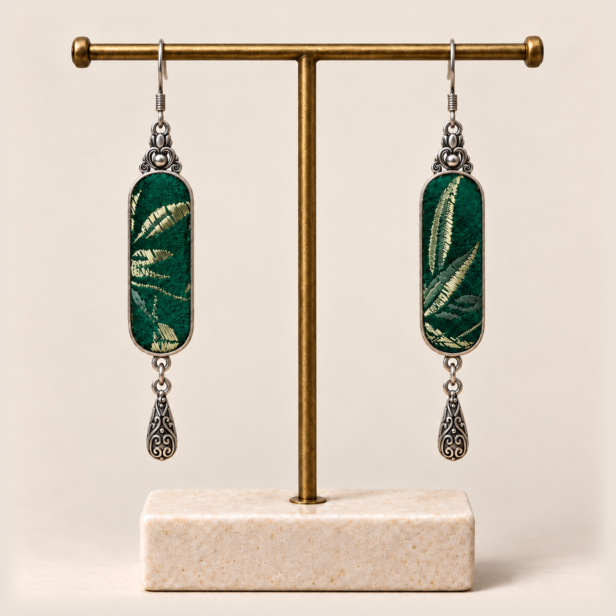 Emerald Reverie Song Brocade earrings hanging from a gold-tone display stand with a pale rectangular base.