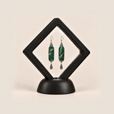 Emerald Reverie earrings inside a black diamond-shaped display frame on a matching base.