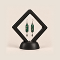 Emerald Reverie earrings inside a black diamond-shaped display frame on a matching base.