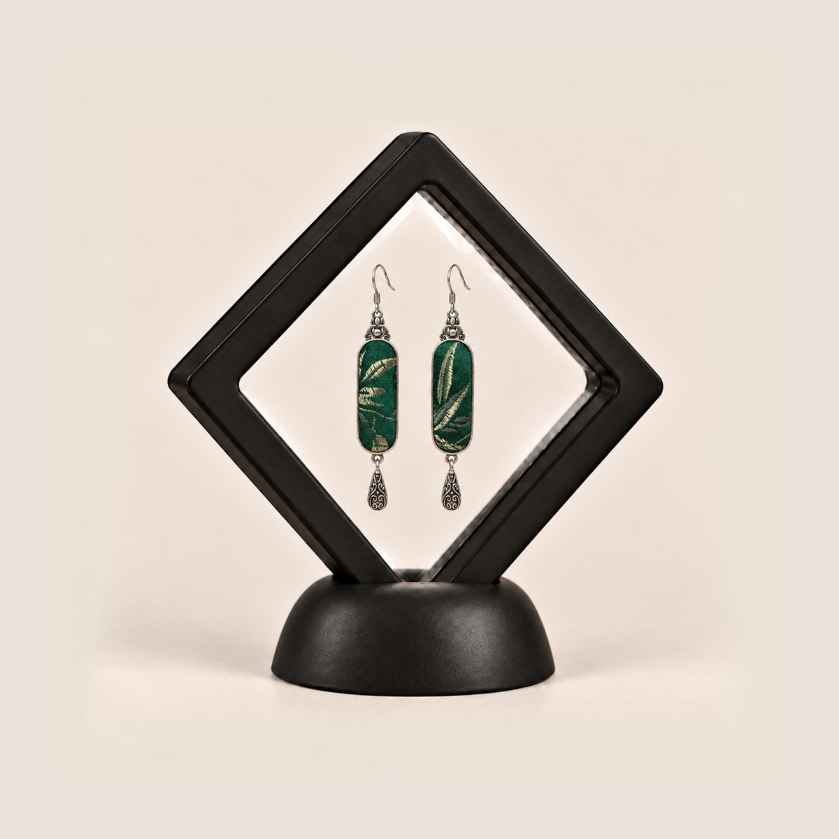 Emerald Reverie earrings inside a black diamond-shaped display frame on a matching base.