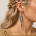 Pastel Arabesque earring worn with pink and green couched embroidery on pale textile facing forward above one teardrop.
